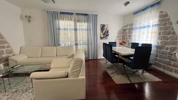 A living room with a sofa, dining table, chairs, and a stone wall.
