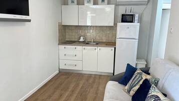 A compact kitchen with white cabinets, a built-in microwave, and a refrigerator.