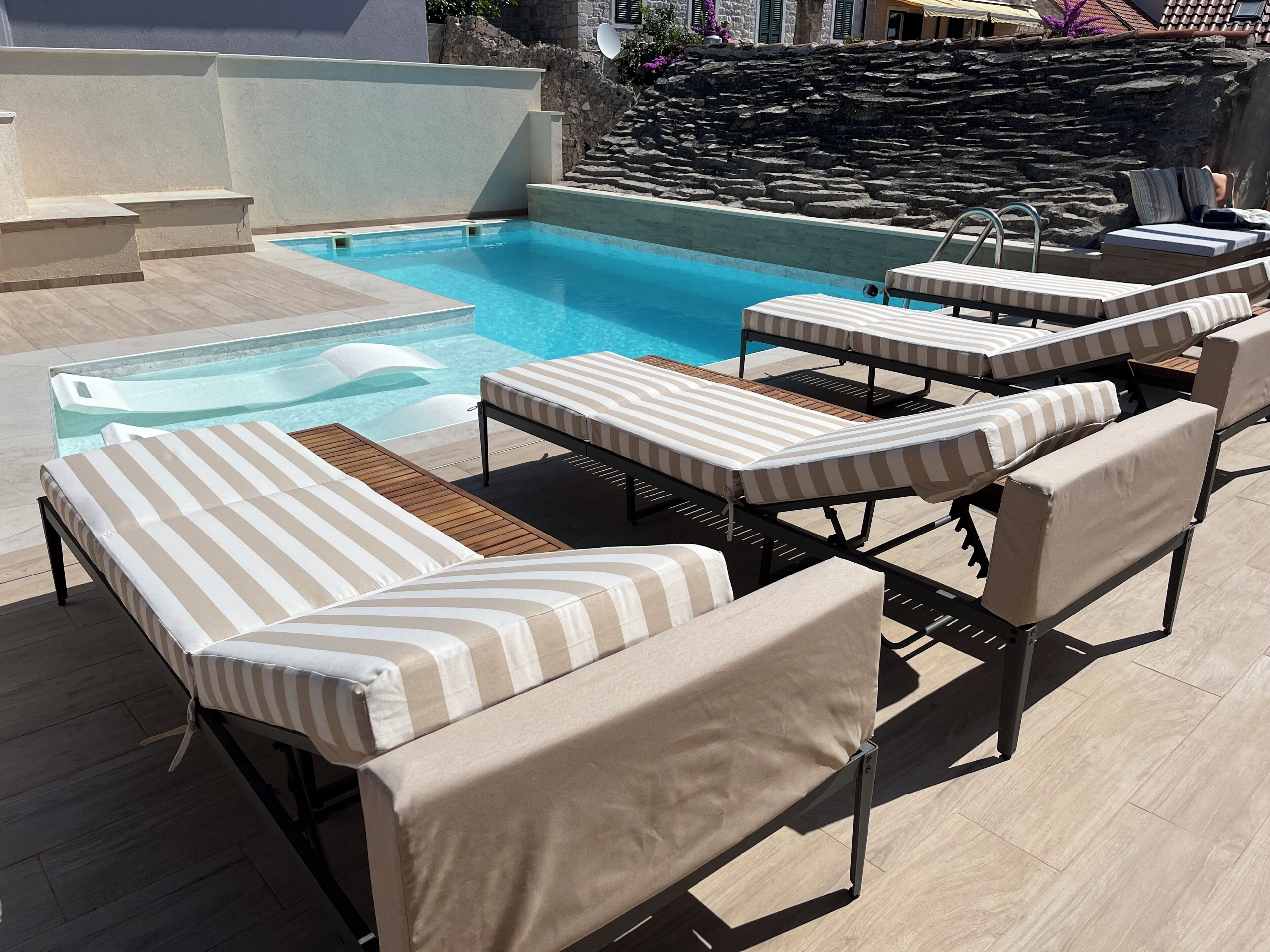 A pool area with lounge chairs and a stone wall.