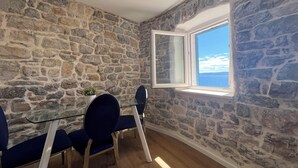 Una stanza con pareti in pietra, un'ampia finestra, un tavolo in vetro e sedie blu.