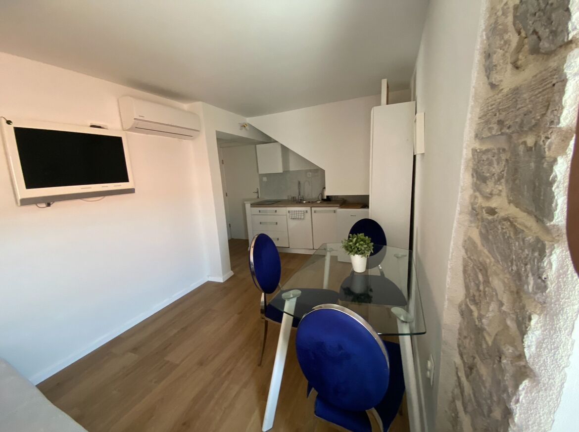 A modern kitchen with white cabinets, a built-in oven, and a glass dining table with blue chairs.