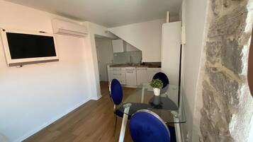 Et moderne køkken med hvide skabe, en indbygget ovn og et glasbord med blå stole.