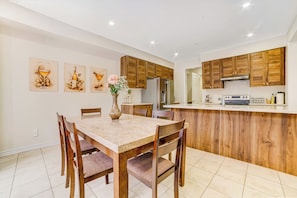 A modern kitchen with wooden cabinets, a dining table with chairs, and a refrigerator. - Modern Luxury 5 ⭐ Space near Brampton | Sleeps 8 (caledon)
