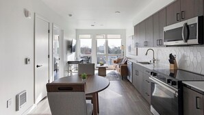 Eine moderne Küche mit Edelstahlgeräten, ein Essbereich mit rundem Tisch und Blick durch große Fenster.