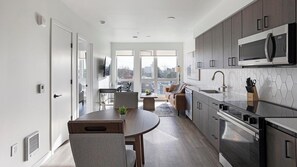 Eine moderne Küche mit Edelstahlgeräten, ein Essbereich mit rundem Tisch und Blick durch große Fenster.