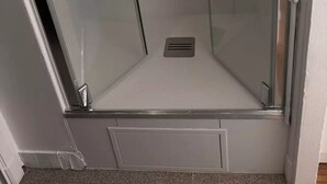 Eine Duschkabine mit Glaswänden und Metallrahmen, einer Dusche und einem Ablaufrinne.