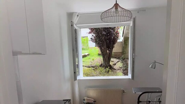 Eine kleine Küche mit Fenster und Heizkörper, ein Bett im angrenzenden Raum.