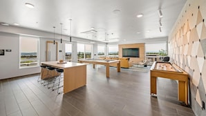 A modern, well-lit room with a pool table, bar area, and seating. Large windows offer views of the outdoors. - Landing | Stunning 1BD, Gym (Seattle)