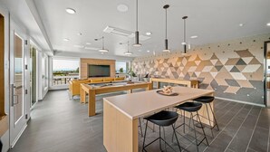 A modern kitchen with a central island, bar stools, and a dining area with a sofa and TV. - Landing | Stunning 1BD, Gym (Seattle)