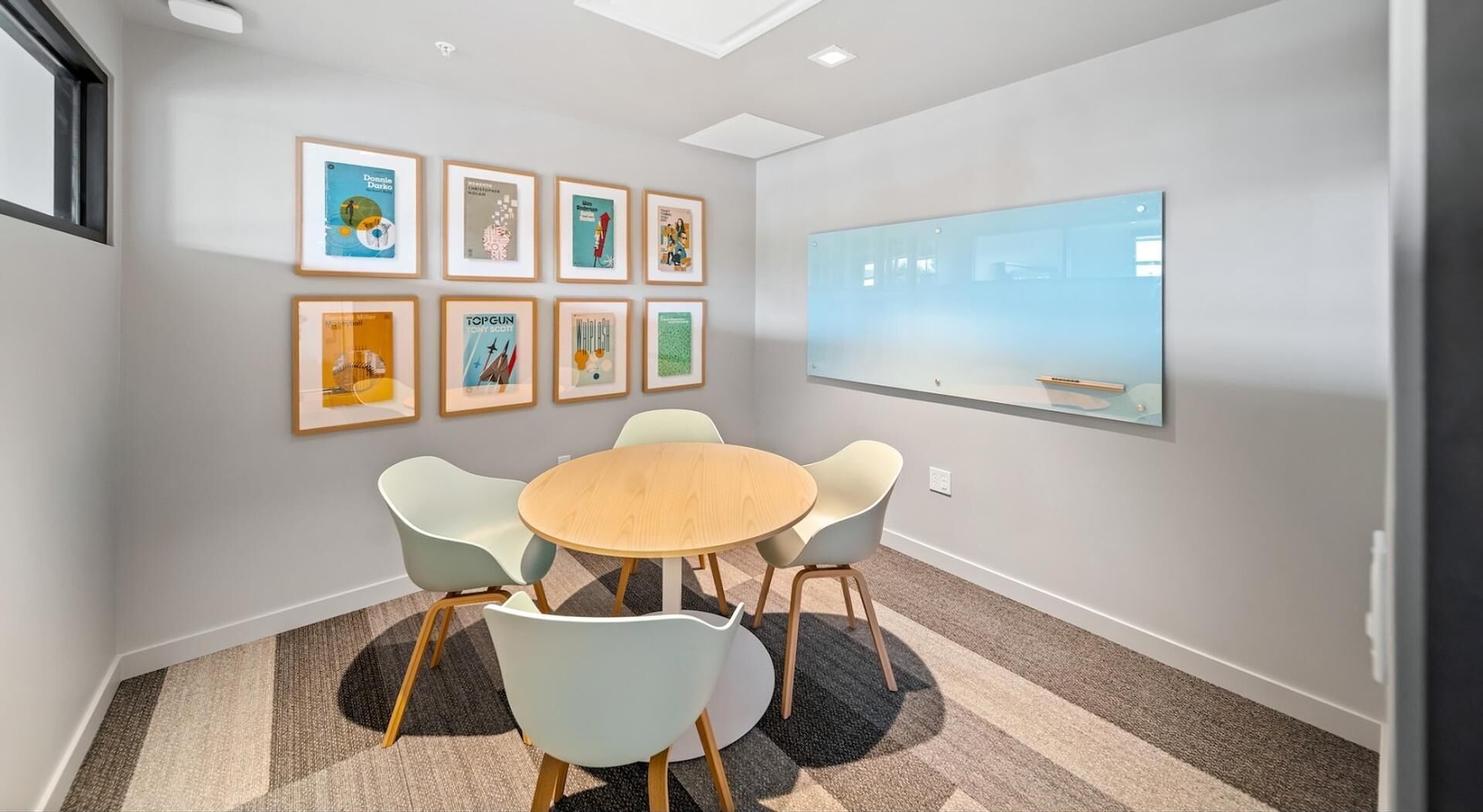 A conference room with a round table, four chairs, and framed artwork on the walls.