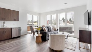 A modern apartment with a kitchen, dining area, and living room. It features large windows, a flat-screen TV, and a minimalist design. - Landing | Incredible 2BD, Gym (Seattle)