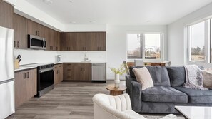 A modern kitchen with dark wood cabinets, a stainless steel refrigerator, and a built-in microwave. - Landing | Incredible 2BD, Gym (Seattle)