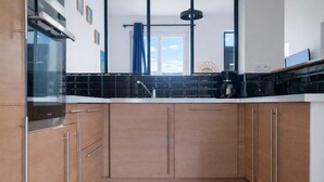 A modern kitchen with wooden cabinets, a black countertop, and a built-in oven. - House near the sea – sleeps 6 people (Les Sables-d´Olonne)