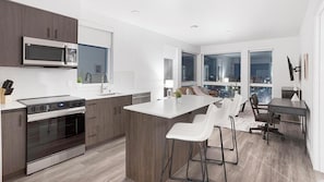 Une cuisine moderne dotée d’un îlot central, de tabourets de bar et d’un coin repas offrant une vue sur la ville la nuit.