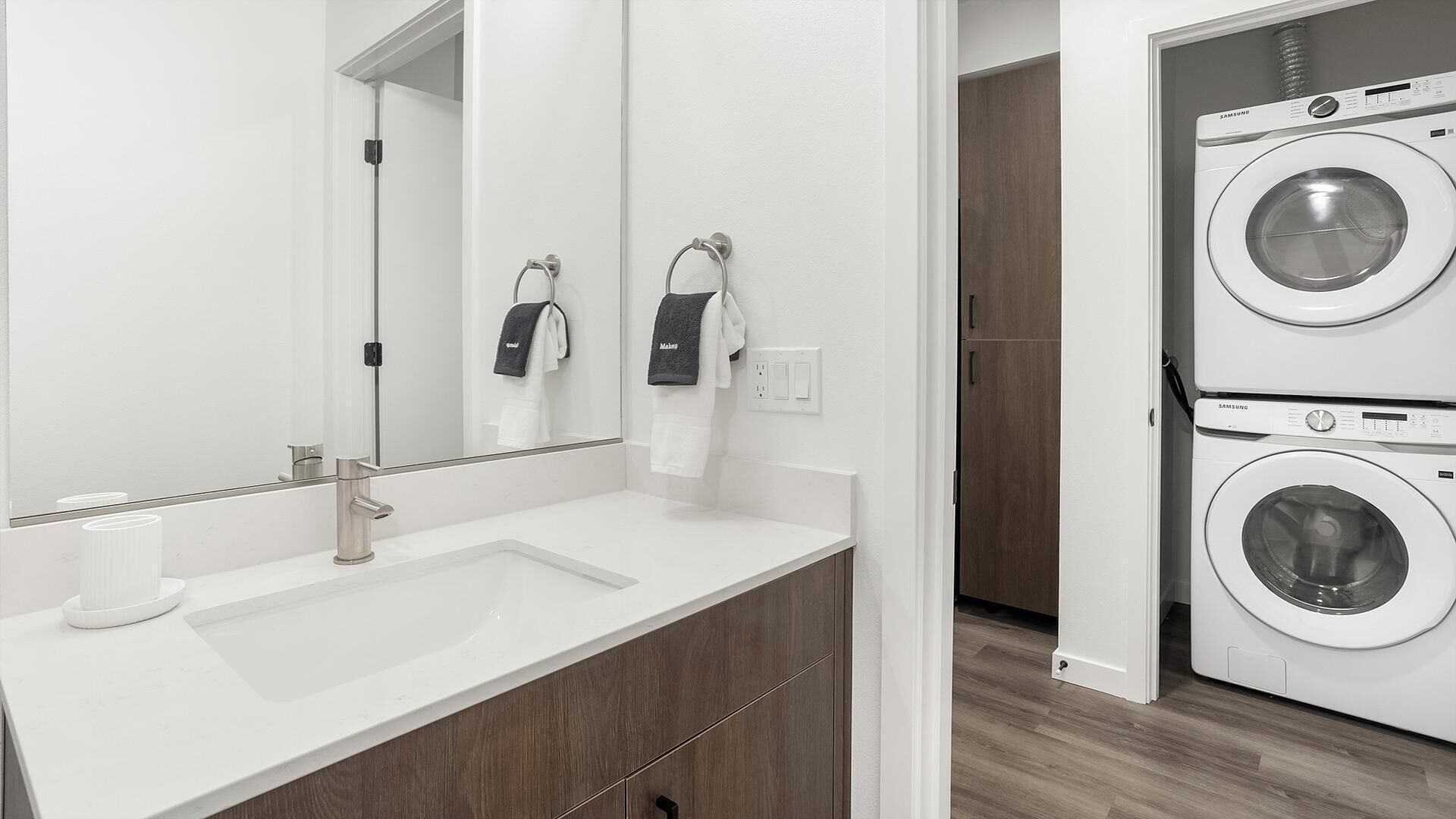 A modern bathroom with a white sink, a mirror, and two stacked Samsung washing machines.