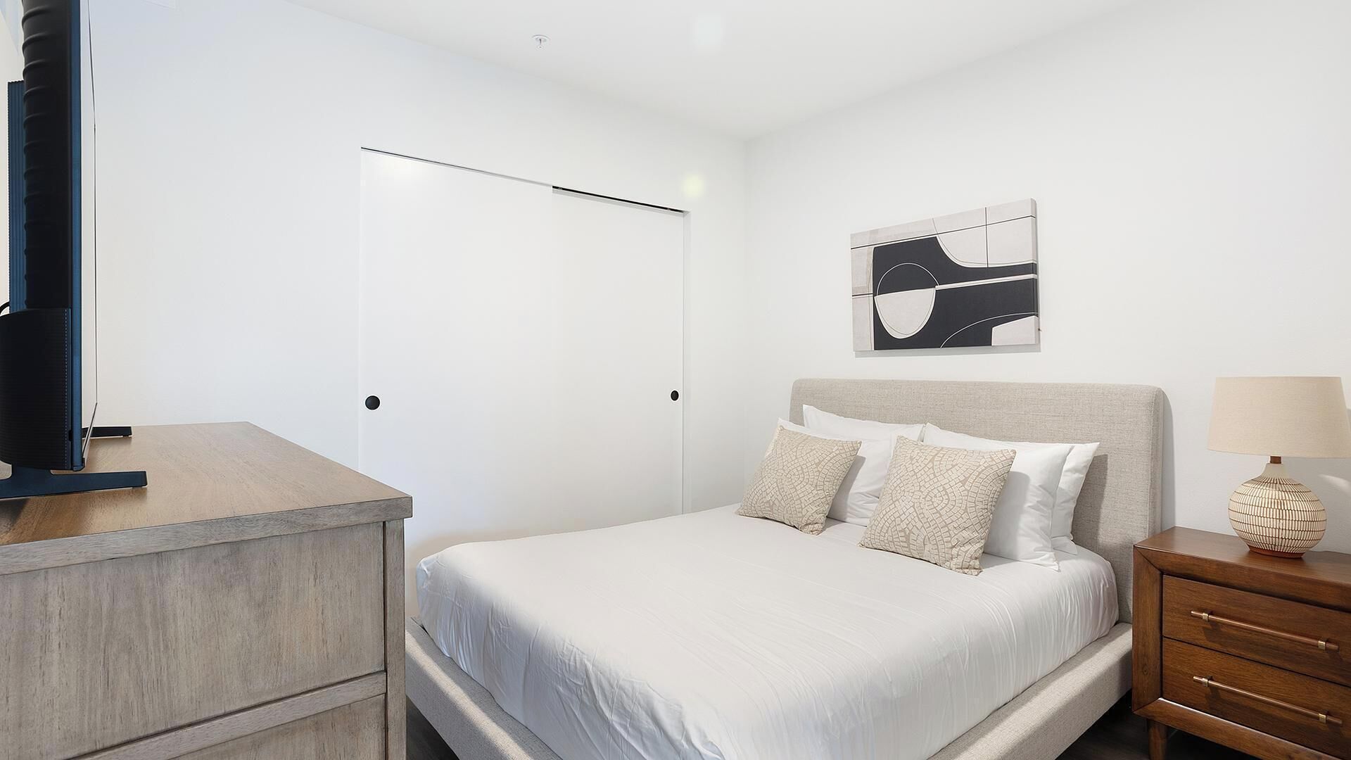 A bedroom with a bed, bedside table, lamp, and a wall-mounted artwork.