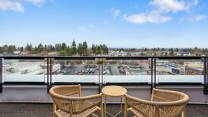 A balcony with wicker furniture and a view of a parking lot and buildings. - Landing | Modern 1BD, Gym (Seattle)