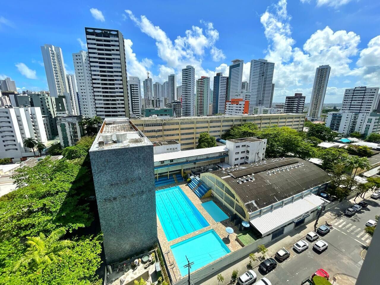 Un edificio alto con area piscina sul tetto, circondato da altri edifici elevati e vegetazione.