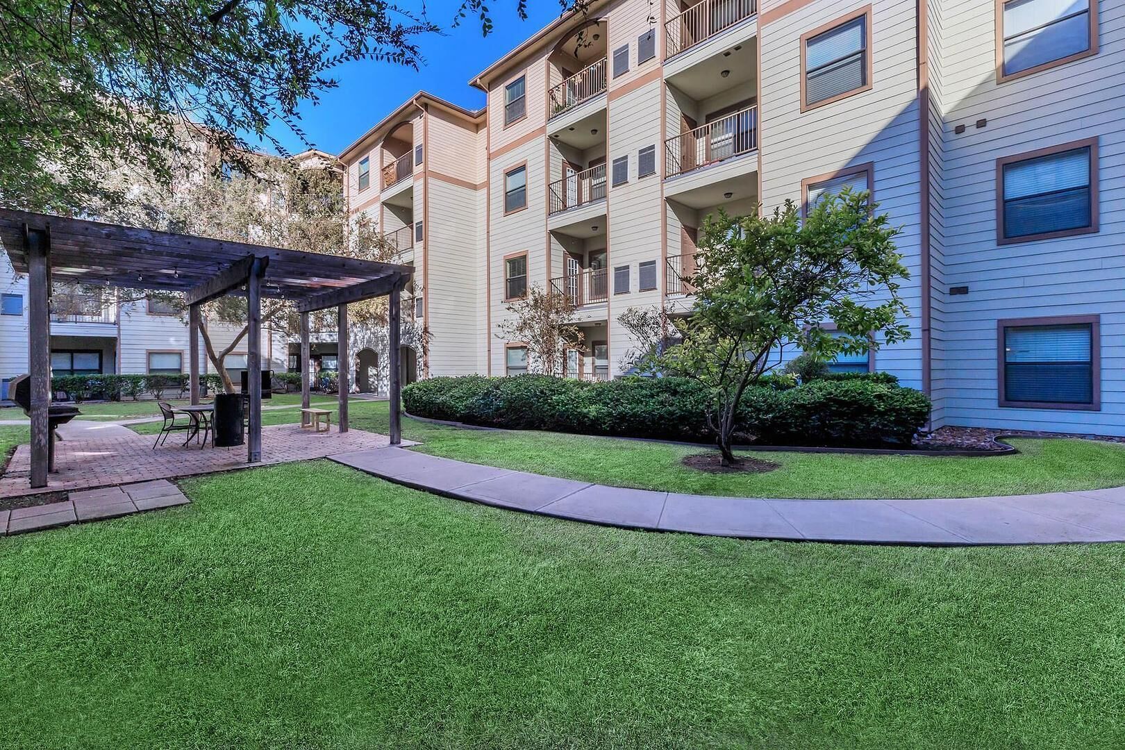A multi-story residential building with a covered outdoor seating area and well-maintained lawn.