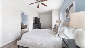 Un dormitorio con cama, ventilador de techo, televisor sobre una cómoda y una lámpara.