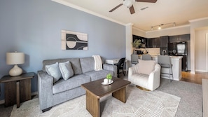A modern living room with a grey sofa, a coffee table, and a dining area with a white chair. - Landing | Modern 1BD, Clubhouse (Corpus Christi)