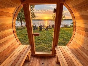 Une cabane en bois dotée d’une fenêtre circulaire donnant sur un paysage lacustre au coucher du soleil.