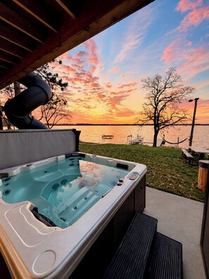 Un bain à remous avec vue sur un coucher de soleil se reflétant sur une étendue d’eau, une table de pique-nique et un arbre en arrière-plan.