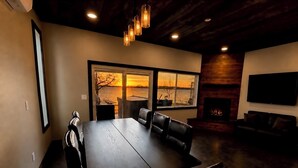 A modern dining area with a large table, chairs, a fireplace, and a TV. - Designer Lake Cabin- PickleBall, HotTub, Slide, EV Charging, Ice Baths, Biking (Dent)