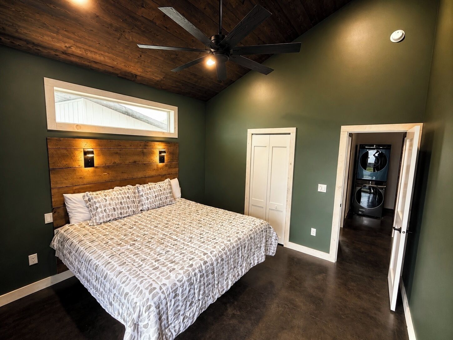 A bedroom with a bed, a ceiling fan, a window, and a door leading to a laundry area.