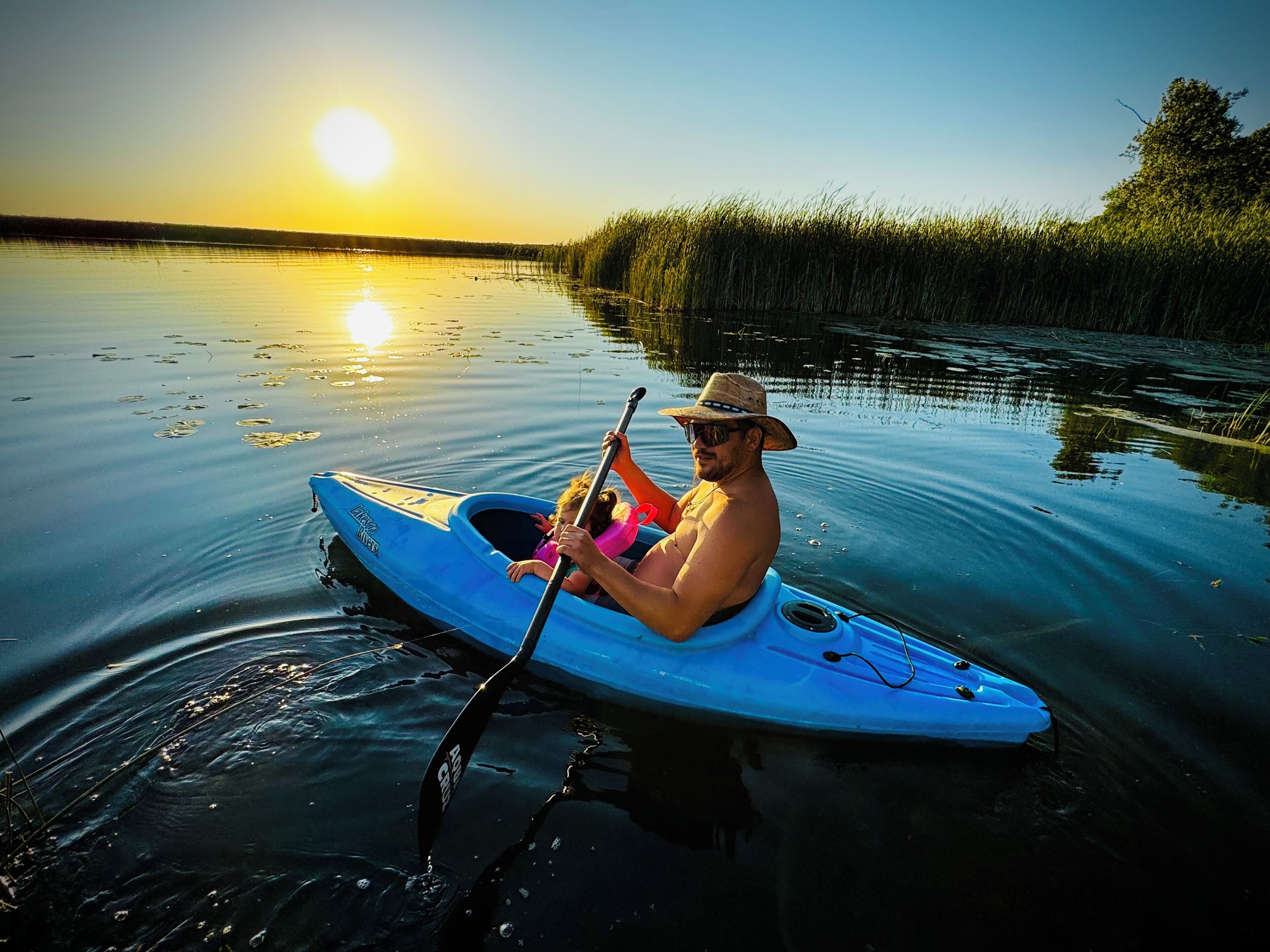 A person in a kayak on calm water with a sunset in the background.
