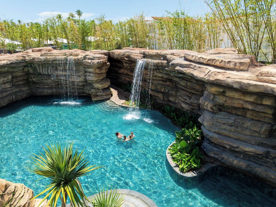 Una piscina con una cascada, rodeada de formaciones rocosas y vegetación.