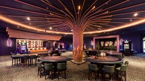 Een moderne bar met diverse speelautomaten, ronde tafels en een decoratieve centrale pilaar.