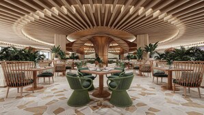 Un vaste espace de restauration intérieur, doté d’un plafond en bois au design moderne, de chaises recouvertes d’un tissu vert et d’une table ronde centrale.