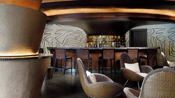 A bar area with wicker chairs, a stone pillar, and a wall with abstract patterns.