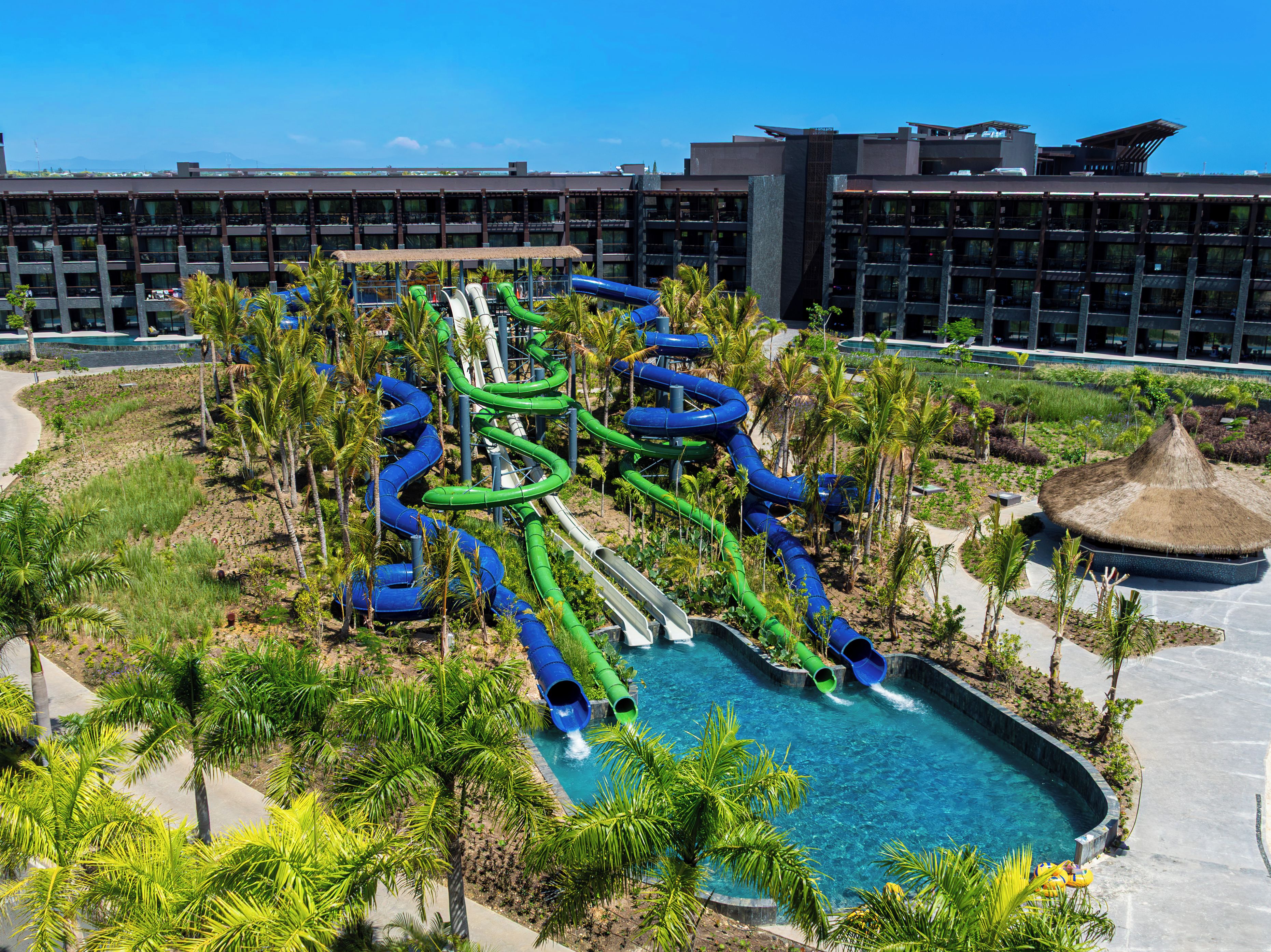 Un parc aquatique doté de nombreux toboggans et d’un espace piscine entouré de palmiers, avec un hôtel en arrière-plan.