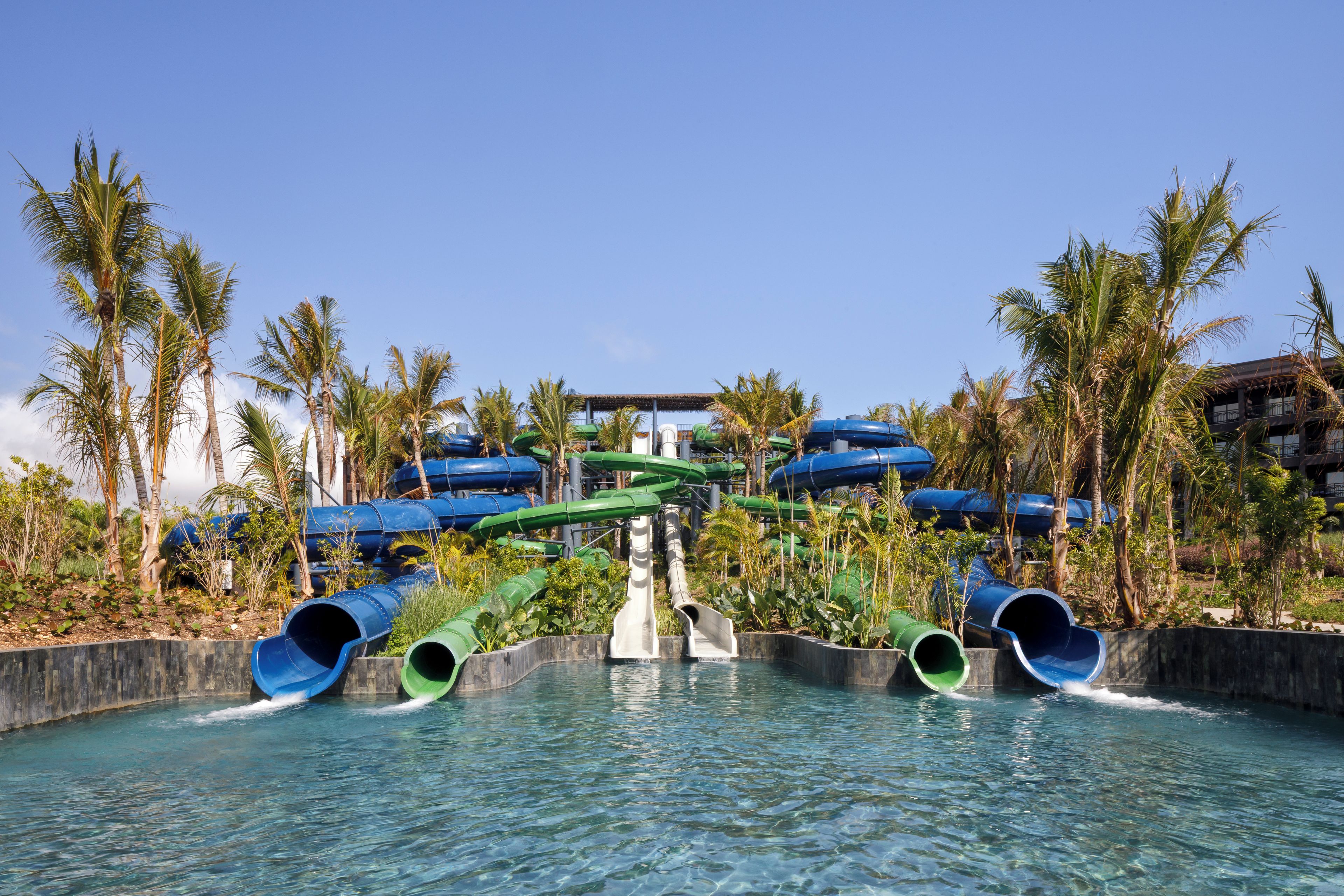 Un parc aquatique doté de nombreux toboggans et de plusieurs piscines, le tout entouré de palmiers.