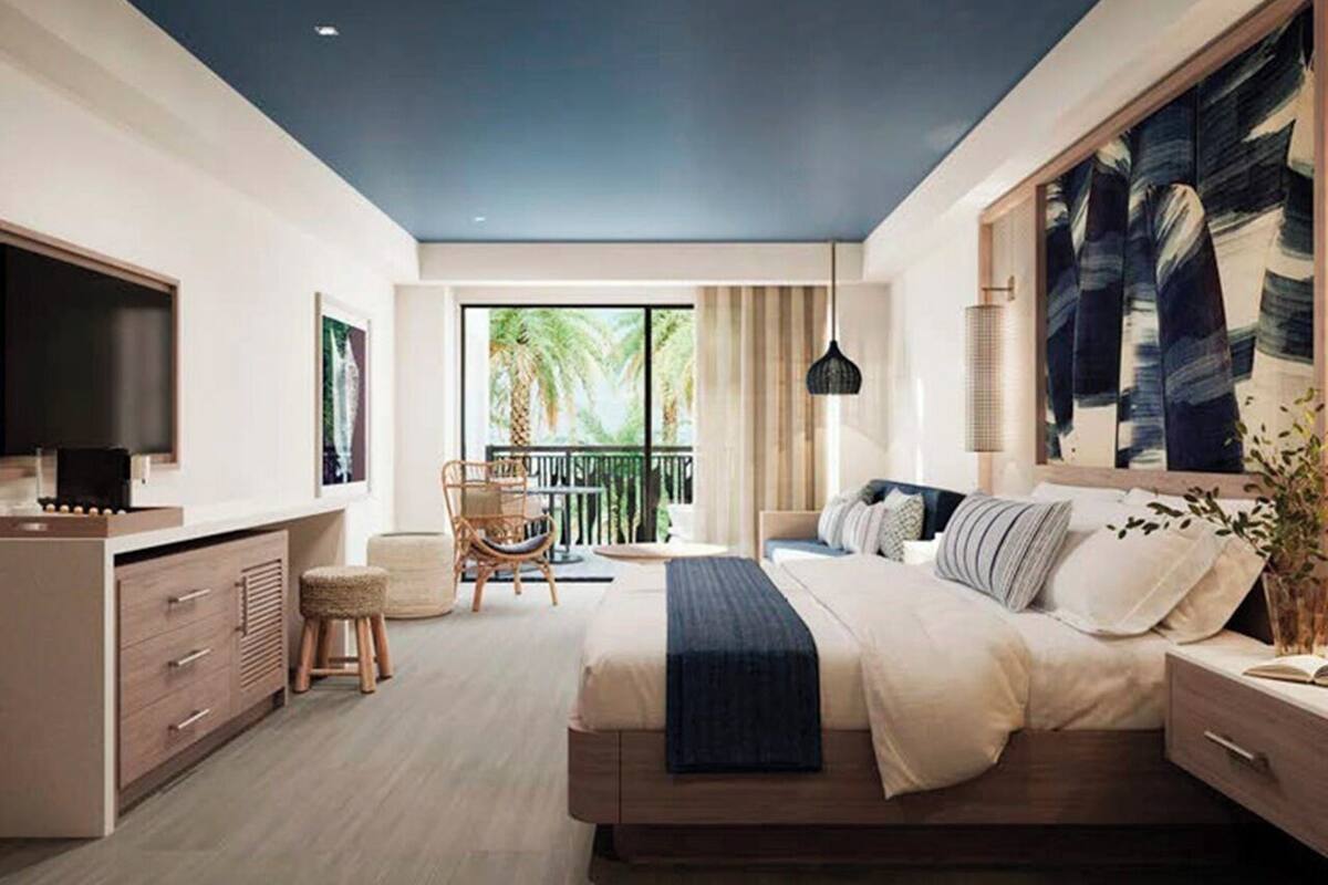 Un dormitorio moderno con una cama grande, un escritorio y una silla. Cuenta con un balcón con vista a palmeras.