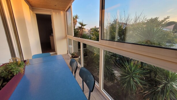 A balcony with a blue table and chairs, large windows, and potted plants. - Appart in solar villa and veranda garden in quiet cul-de-sac - 8mn from the sea (Lattes)