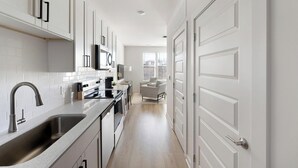Una cocina moderna con armarios blancos, un lavamanos de acero inoxidable y una zona de comedor con una silla.