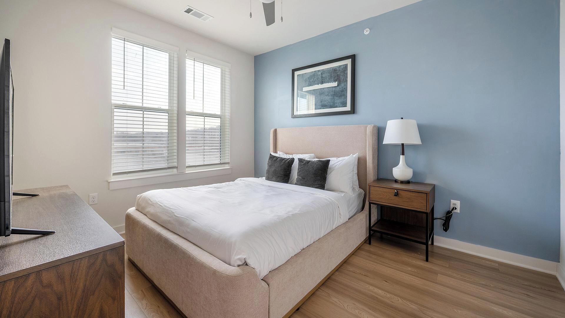 A bedroom with a bed, bedside table, lamp, and a framed picture on the wall.