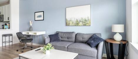 Ett modernt vardagsrum med en grå soffa, ett vitt soffbord och ett litet sidobord med en lampa.