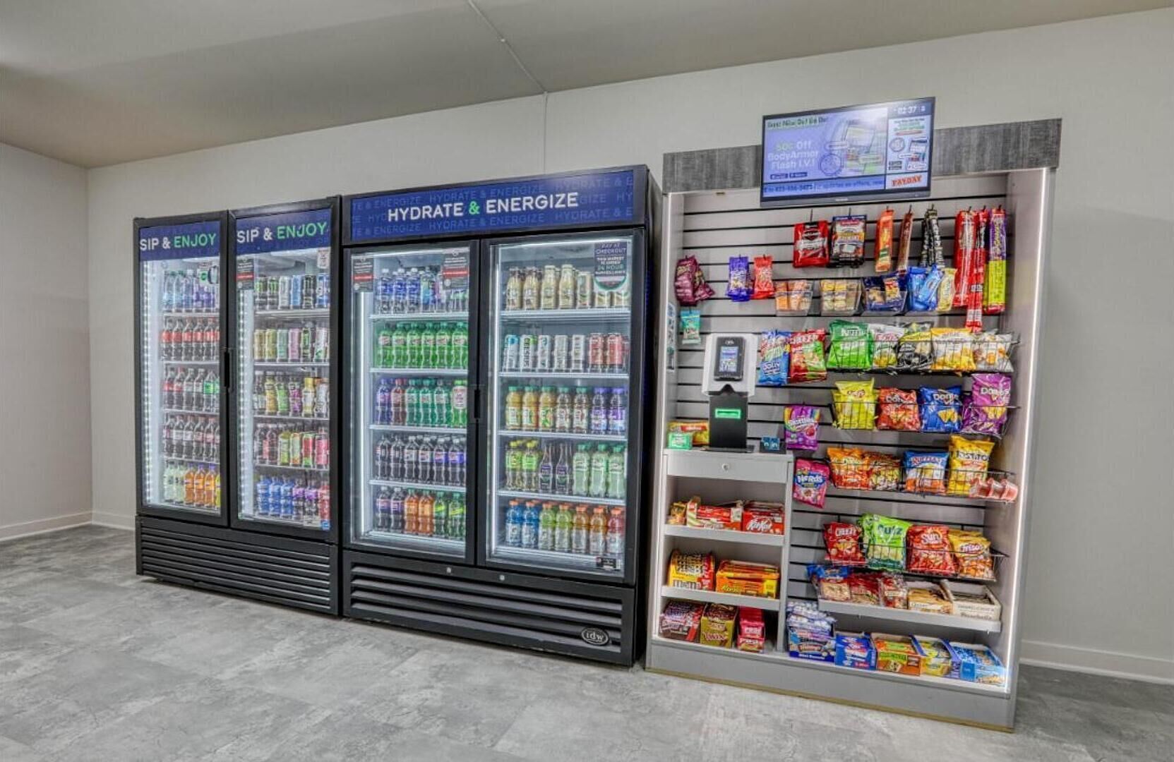 Drei Getränkespender mit den Aufschriften „Sip & Enjoy“ und „Hydrate & Energize“ bieten eine Auswahl an Getränken. Daneben befindet sich eine Snackauslage mit verschiedenen verpackten Snacks.
