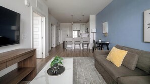Una sala de estar moderna con un televisor de pantalla plana, un sofá gris con un cojín amarillo, una mesa de centro con una planta y una alfombra estampada.