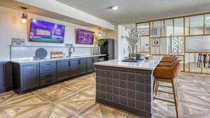 A modern kitchen with a large island, dark cabinetry, and a herringbone-patterned floor. - Landing | Spectacular 2BD, Pool, Game Room (Knoxville)