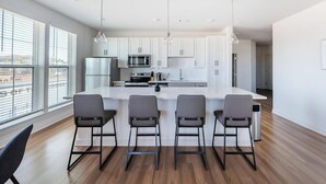 A modern kitchen with white cabinets, a central island with bar stools, and pendant lighting. - Landing | Beautiful 2BD, Game Room, Pool (Knoxville)