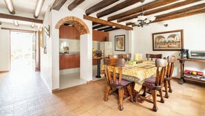 A dining area with a wooden table and chairs, a kitchen in the background, and a doorway leading to another room.
