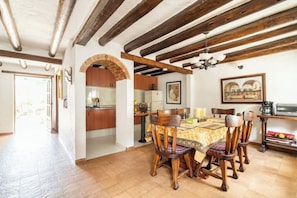 A dining area with a wooden table and chairs, a kitchen in the background, and a doorway leading to another room.