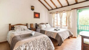 A bedroom with two beds, wooden beams on the ceiling, a nightstand, a framed picture, and a window with curtains.