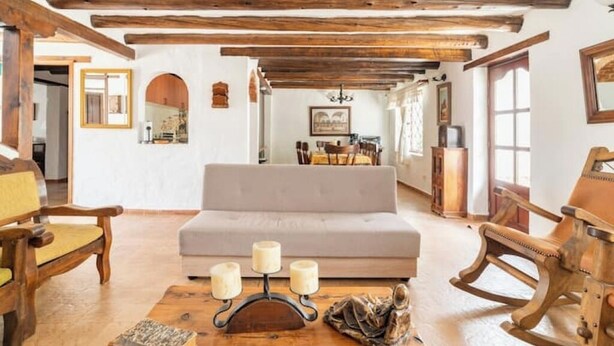 A cozy room with a sofa, wooden rocking chairs, a coffee table with candles, and exposed wooden beams on the ceiling.