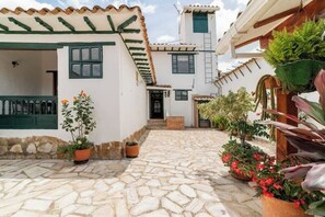 A courtyard with stone flooring, white buildings with green accents, and potted plants.